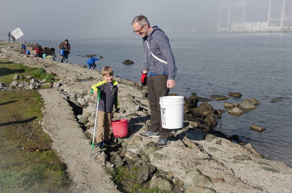 Father and young son holding pickers and buckets doing a shoreline cleanup