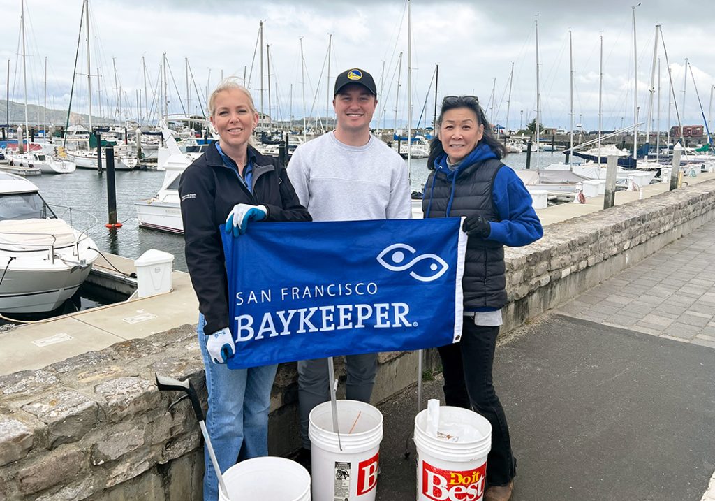 Three cleanup volunteers with buckets and Baykeeper banner
