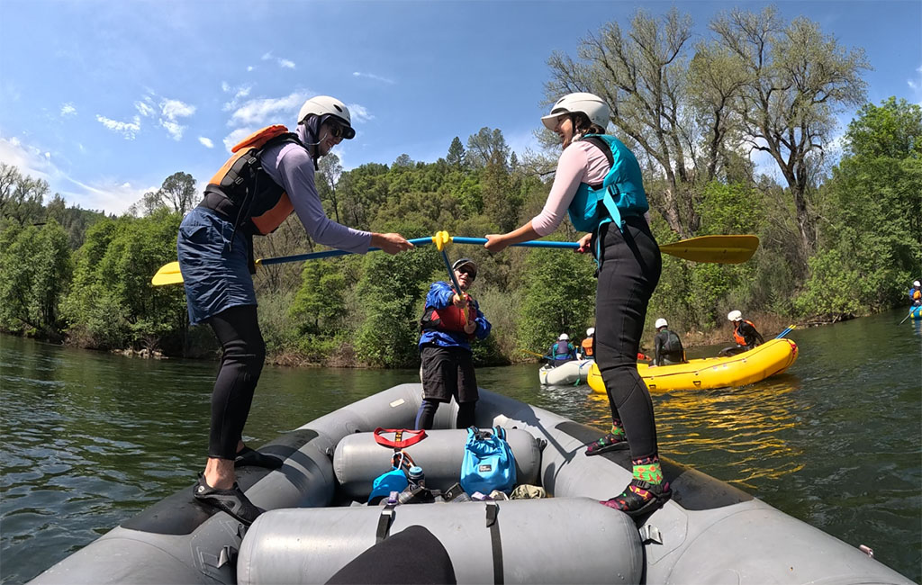 Two people on a raft with oars raised on the American River