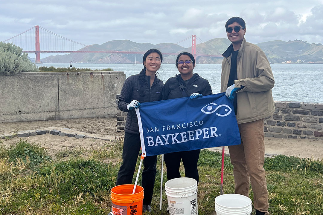 Three trash volunteers along the Bay holding a Baykeeper banner