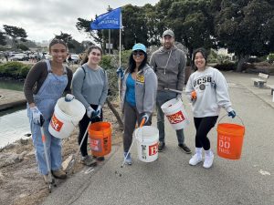 Volunteers smiling at a shoreline cleanup with buckets and pickers