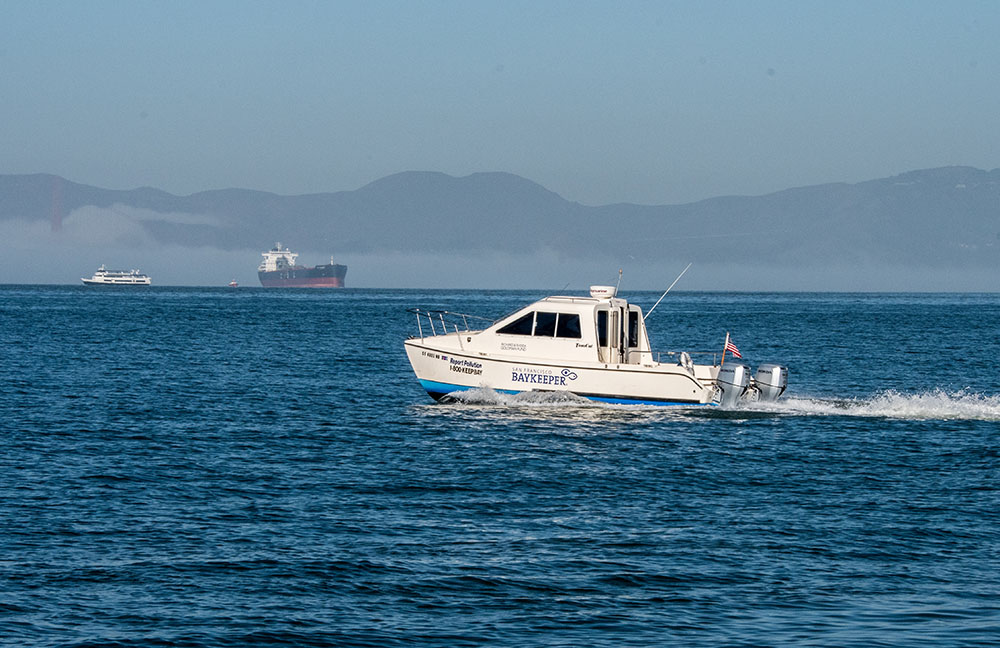 The Baykeeper patrol boat on the Bay with a container ship in the background
