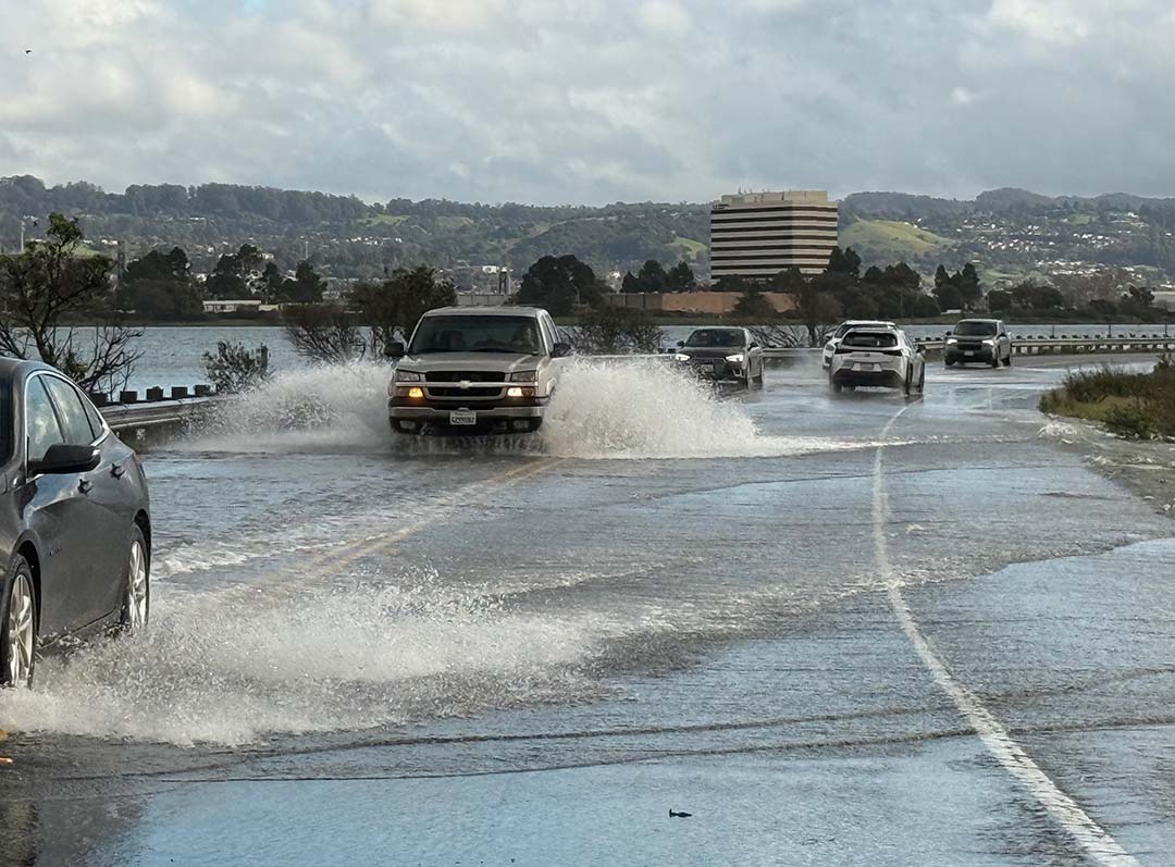 Cars driving through a flooded road during the King Tides