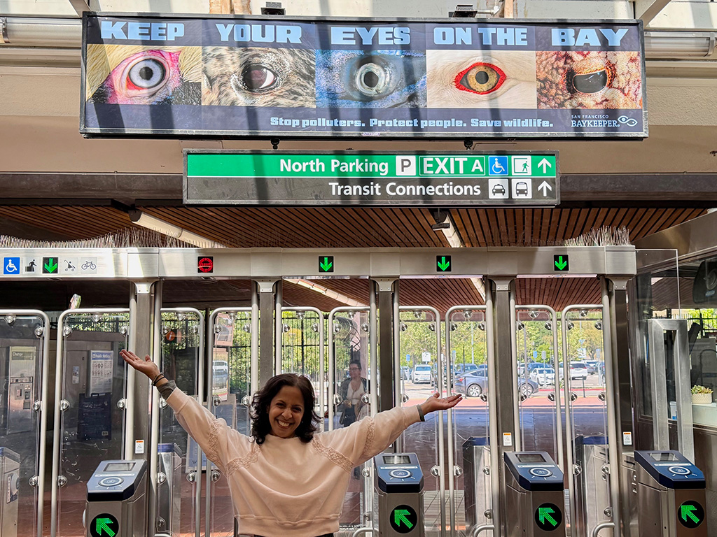 Baykeeper director Sejal Choksi-Chugh with arms outstretched under a sign reading: Keep Your Eyes on the Bay