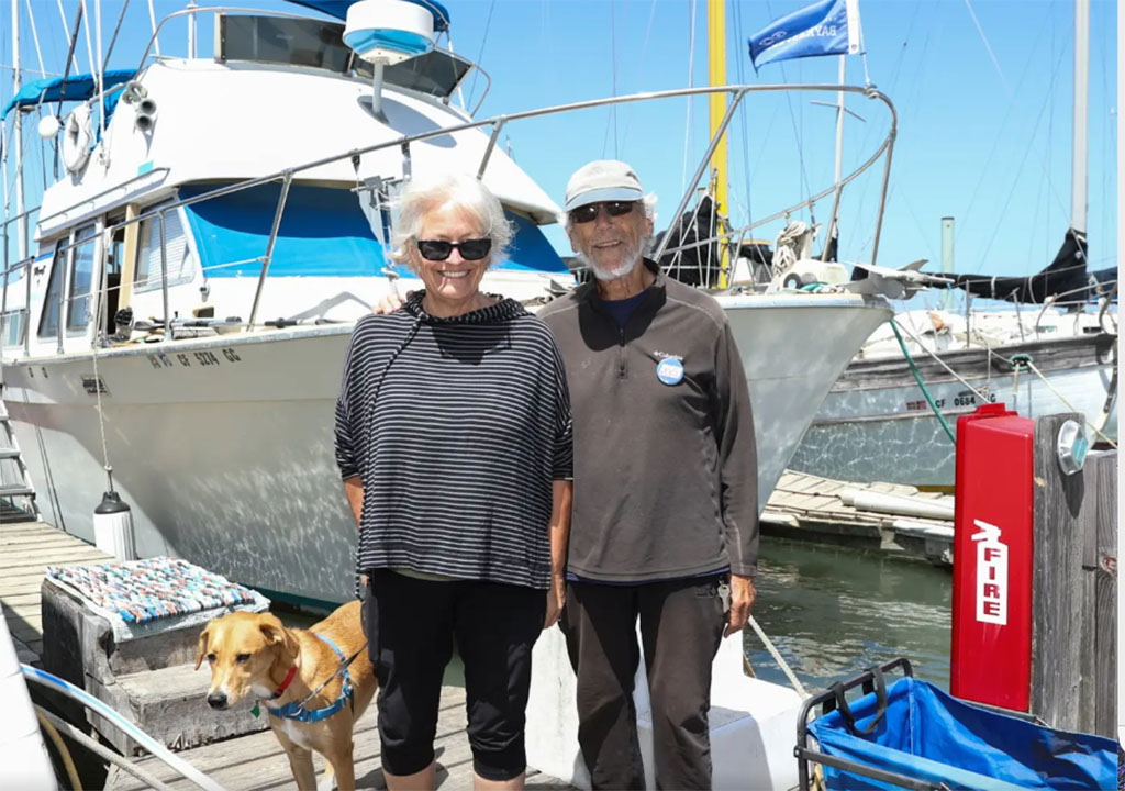 Two people standing on a dock in front of a boat smiling